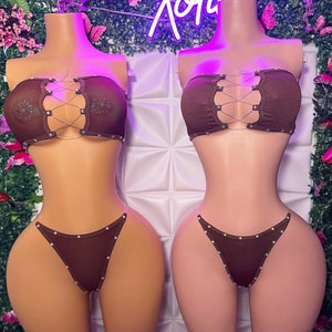 Puede incluir: Dos conjuntos de lencería marrones con un diseño de cruz y pedrería. Los conjuntos incluyen un top sin tirantes y una tanga.