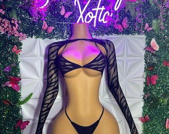 May include: Black lingerie set displayed on a mannequin. The set comprises a triangle bra, a thong, and a long-sleeved, open-front top. A neon sign reading "San Diego Xotic" is in the background, surrounded by flowers and butterflies.