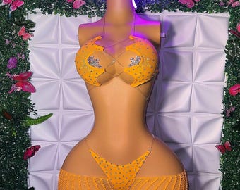 Op de afbeelding: Een feloranje tweedelige bikiniset met een haltertop met doorzichtige bandjes, ingewikkelde vetersluiting en zilveren strass-versieringen. Het bijpassende broekje heeft een string-model met strass-steentjes en een transparante mesh-laag.