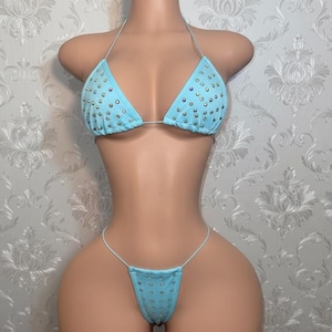 May include: A light blue bikini set featuring a triangle top and matching bottom, both adorned with scattered iridescent rhinestones. The top has thin halter straps, and the bottom features thin side ties, creating a coordinated two-piece swimwear set.