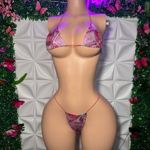 Könnte beinhalten: Ein zweiteiliges Bikini-Set mit Gelddruck-Design. Das Oberteil ist im Dreiecksstil mit dünnen Trägern, und das Unterteil ist im String-Stil. Der Bikini wird auf einer Schaufensterpuppe präsentiert.