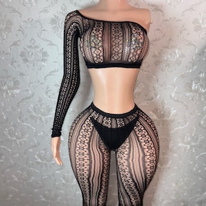 May include: Black lingerie set featuring a one-shoulder crop top with a long sleeve and matching high-waisted leggings. The set is made of a delicate, open-weave fabric with a floral pattern. The top has a sequined design.