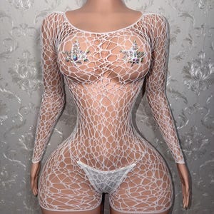 May include: A white long-sleeve fishnet bodysuit featuring an irregular, web-like pattern throughout the garment. The piece includes two decorative, star-shaped embellishments adorned with iridescent, multi-colored crystals at the chest area.