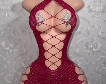 May include: A deep red, sleeveless, form-fitting mini dress featuring a fishnet-style cutout pattern across the front and sides. The garment is embellished with small, scattered clear rhinestones and two clusters of iridescent crystals at the chest.