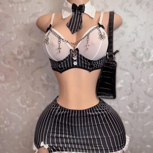 May include: A lingerie set on a mannequin featuring a white and black striped bra and skirt. The bra has chain detailing and a matching collar and tie. A black purse hangs on the mannequin's shoulder.