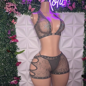 May include: A two-piece lingerie set in a dark green color with a mesh fabric and rhinestones. The top is a halter style with a clasp closure in the front. The shorts have a high-waisted fit with cutouts on the sides.