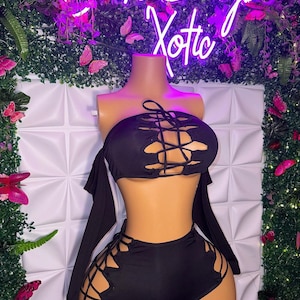 Puede incluir: Conjunto negro de dos piezas con un diseño de encaje. La parte superior es de estilo bandeau con mangas largas y la parte inferior es un short de cintura alta.