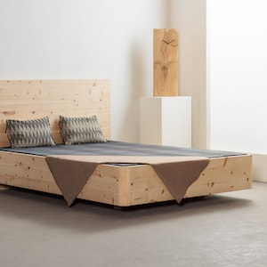 Pode incluir: Uma estrutura de cama de madeira com acabamento em madeira clara. A cama tem cabeceira e pé de cama, e é feita de madeira maciça. A cama está coberta com um cobertor cinza e duas almofadas com um padrão geométrico.
