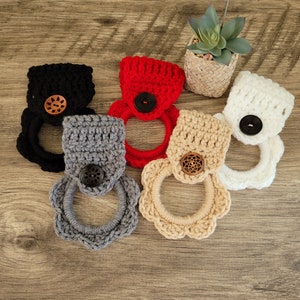 May include: Five crocheted dishcloths with wooden buttons. The dishcloths are in various colors, including red, black, white, gray, and beige.