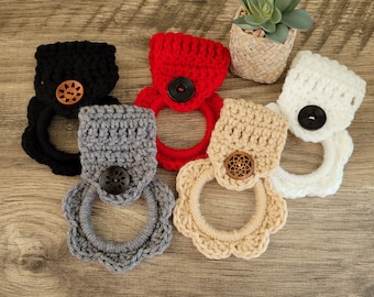 May include: Five crocheted dishcloths with wooden buttons. The dishcloths are in various colors, including red, black, white, gray, and beige.