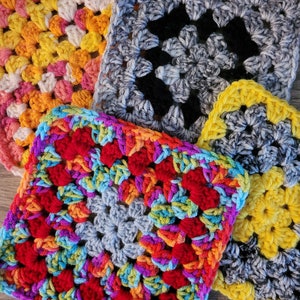 May include: Four crocheted squares in different colors and patterns. The squares are made with a variety of yarn colors, including yellow, pink, red, blue, green, and gray. The squares are arranged in a pile, with the yellow square on top.