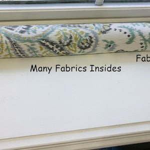 May include: A white window draft stopper with a patterned fabric cover. The fabric has a paisley design in shades of green, gray, and yellow. The text "Many Fabrics Insides" and "Fabric 2" is visible on the white surface below the draft stopper.