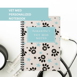 May include: A light blue notebook with a white background and a pattern of black paw prints and blue stars. The notebook says "Samantha's Vet Med Notes" in a white rectangle on a light blue background.