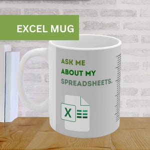 Puede incluir: Taza de cerámica blanca con el texto "EXCEL MUG" en una pancarta verde. La taza presenta la frase "ASK ME ABOUT MY SPREADSHEETS" y un icono de Excel. Una lista de atajos de Excel está impresa en el lateral.