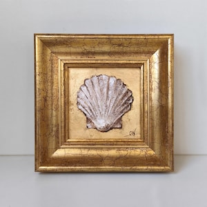 Könnte beinhalten: Ein quadratisches Wandbild mit einer strukturierten weißen Muschel auf einem Blattgoldhintergrund. Das Kunstwerk ist in einem breiten, verzierten Goldrahmen mit einer gealterten, rissigen Oberfläche gefasst. Eine kleine schwarze Signatur ist sichtbar.