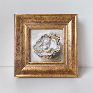 May include: Square framed painting of an oyster with a pearl. The oyster is painted in shades of white, gray, and gold, with a large, round pearl in the center. The frame is gold with a distressed finish.
