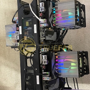 Könnte beinhalten: Ein schwarzes Computergehäuse mit zwei Motherboards und zwei CPU-Kühlern. Die Kühler haben RGB-Beleuchtung und sind vertikal montiert. Das Gehäuse steht auf einer weißen Oberfläche.