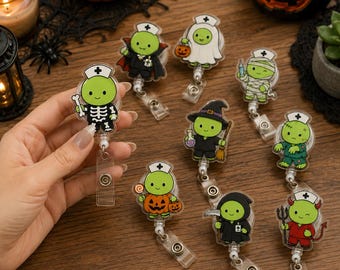Op de afbeelding: Een verzameling van negen acryl badgehouders met groene stripfiguren in diverse Halloween-kostuums, waaronder een skelet, vampier, geest, mummie, heks, pompoen, magere hein, zombie en duivel, elk voorzien van een verpleegsterskapje.