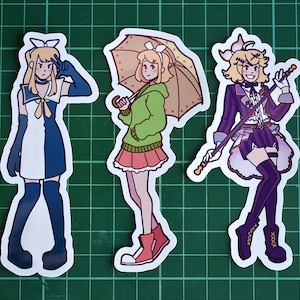 May include: Three colorful anime-style character stickers. The first sticker features a girl with blue hair and a white and blue dress. The second sticker features a girl with yellow hair and a green sweater and a pink skirt. The third sticker features a girl with yellow hair and a purple dress and a black and white striped shirt.