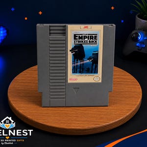 May include: A gray Nintendo Entertainment System game cartridge for The Empire Strikes Back. The label features a blue-toned illustration of AT-AT walkers on a snowy landscape, with the JVC, Lucasfilm Games, and Nintendo logos clearly visible.