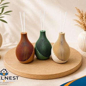 Könnte beinhalten: Drei dekorative Schilfrohrdiffusoren in Braun-, Grün- und Cremetönen, jeweils mit weißen Schilfrohren. Die Diffusoren haben ein geripptes Design und sind auf einem Holztablett angeordnet. Weitere dekorative Elemente sind Vasen, Pflanzen und eine brennende Kerze.