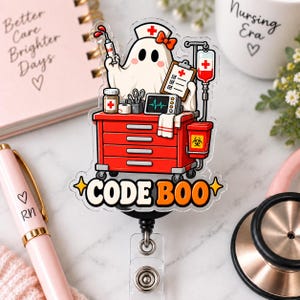 May include: A clear acrylic badge reel featuring a cartoon ghost dressed as a nurse with a red bow, standing behind a red medical cart with a syringe, clipboard, monitor, and IV bag. The text CODE BOO is printed in bold black and orange letters.