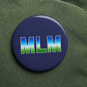 May include: A round, navy blue button with the letters "MLM" in a gradient of blue and green. The button is attached to a green backpack, with a zipper and other details visible.
