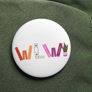 Könnte beinhalten: Ein weißer Ansteckbutton mit den Buchstaben "WWW" und farbenfrohen Illustrationen von Büchern, einem Ordner und einer Pflanze. Der Button ist an einem grünen Rucksack befestigt.