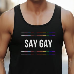 May include: Black tank top with the text "SAY GAY" in white letters. The text is centred on the shirt and is surrounded by three horizontal lines. The lines are rainbow coloured.