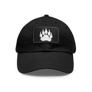 Puede incluir: Gorra de béisbol negra con un parche de pata de oso blanca en la parte delantera.