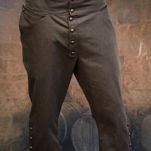 Könnte beinhalten: Braune, hochgeschnittene Hose mit Knopfleiste und mehreren Knöpfen an der Vorder- und den Seiten. Die Hose ist knapp unterhalb des Knies abgeschnitten.
