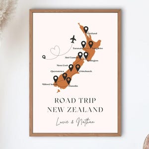 Peut inclure: Impression encadrée d'une carte de la Nouvelle-Zélande avec des marqueurs de localisation. Le texte "ROAD TRIP NEW ZEALAND" est affiché en dessous, avec les noms "Lucie & Nathan". La carte est de couleur marron chaud.