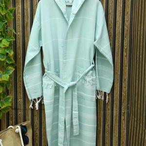 May include: A light green hooded bathrobe with white stripes and fringe trim. The robe has a tie belt and two pockets.