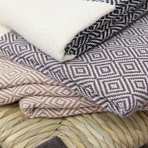 Pu&ograve; includere: Una pila di tre coperte tessute con motivi geometrici. La coperta superiore &egrave; bianca con forme di diamanti neri, la coperta centrale &egrave; marrone con forme di diamanti bianchi e la coperta inferiore &egrave; bianca con forme di diamanti marroni.