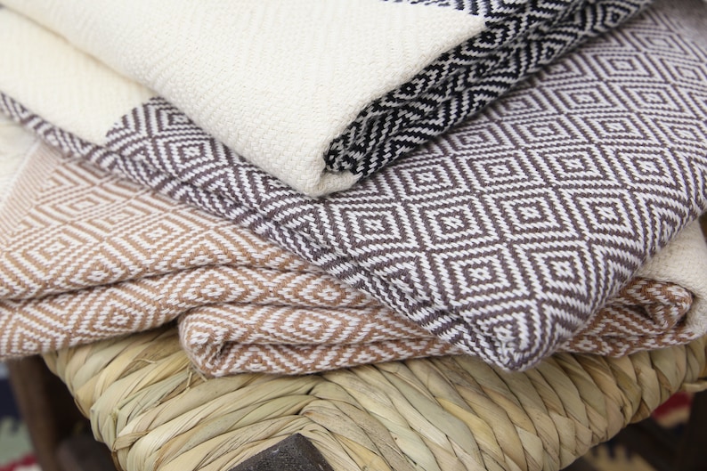 Pu&ograve; includere: Una pila di tre coperte tessute con motivi geometrici. La coperta superiore &egrave; bianca con forme di diamanti neri, la coperta centrale &egrave; marrone con forme di diamanti bianchi e la coperta inferiore &egrave; bianca con forme di diamanti marroni.