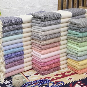 Pu&ograve; includere: Una pila di asciugamani turchi colorati con un motivo a rombi. Gli asciugamani sono piegati e impilati in una variet&agrave; di colori, tra cui blu, verde, rosa e giallo.