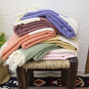 Pu&ograve; includere: Una pila di sei asciugamani turchi colorati con un motivo a rombi, piegati e disposti su uno sgabello di legno. Gli asciugamani sono in tonalit&agrave; di blu, rosso, arancio, verde e rosa.