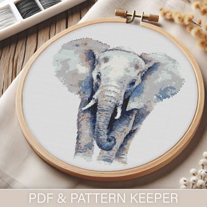 May include: A cross-stitch embroidery of an elephant in a wooden embroidery hoop. The elephant is white with blue and grey shading. The embroidery is on a white fabric.
