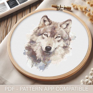 Puede incluir: Bordado de punto de cruz de la cabeza de un lobo en un aro de madera. El lobo está representado en tonos marrones, grises y blancos, con un efecto acuarela. El texto "PDF - PATTERN APP COMPATIBLE" está en la parte inferior.