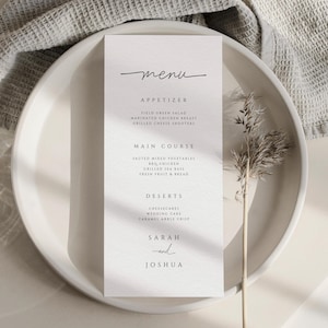 Może przedstawiać: Minimalistyczna karta menu weselnego ze słowem "menu" w eleganckim skrypcie. Menu zawiera przystawki, dania główne i desery, z nazwiskami "Sarah" i "Joshua" na dole. Karta znajduje się na białym talerzu z gałązką suchej trawy.