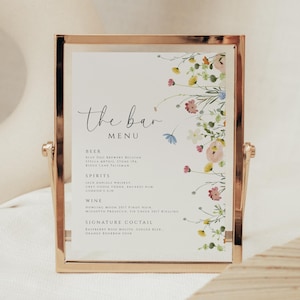 May include: A gold-coloured framed bar menu with floral decorations. The menu has a handwritten font with categories for beer, spirits, wine, and signature cocktails. The floral design includes pink, yellow, and blue flowers.