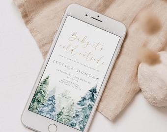 May include: A smartphone displaying a baby shower invitation with a watercolor background of pine trees and the text "Baby it's cold outside" in gold lettering. The invitation is for Jessica Duncan on Saturday, December 16 at 3:00 PM at Sophie's House in San Diego, CA 12345.