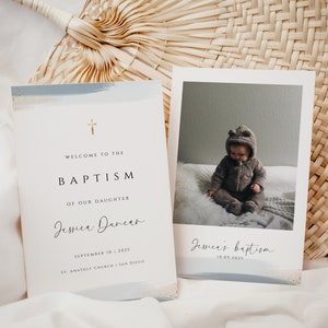 Könnte beinhalten: Eine Taufeinladungskarte mit blauem Aquarellhintergrund und goldenem Kreuz. Die Karte enthält den Text "Willkommen zur Taufe unserer Tochter Jessica Duncan 10. September 2025 St. Anatoly Church | San Diego". Eine separate Karte zeigt ein Foto eines Babys in einem braunen Kapuzenoutfit, das auf einem weißen Bett sitzt. Der Text "Jessicas Taufe 10.09.2025" steht auf der Karte.