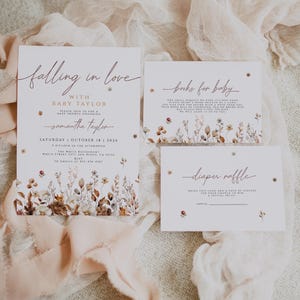 May include: Baby shower invitations with floral accents. The invitation reads "Falling in love with Baby Taylor" and includes details for the event. Additional cards request books and a diaper raffle. Soft peach ribbon and floral details.