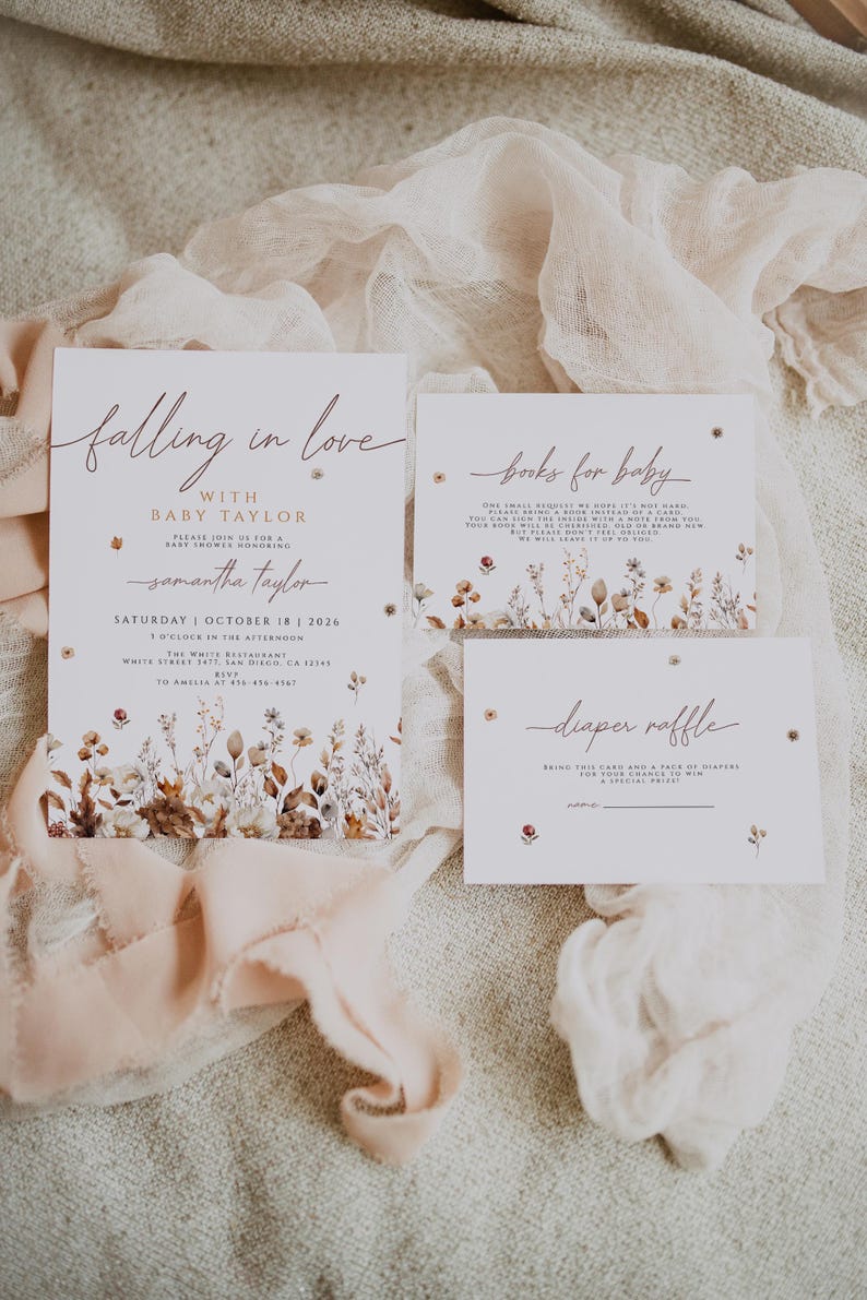 May include: Baby shower invitations with floral accents. The invitation reads "Falling in love with Baby Taylor" and includes details for the event. Additional cards request books and a diaper raffle. Soft peach ribbon and floral details.