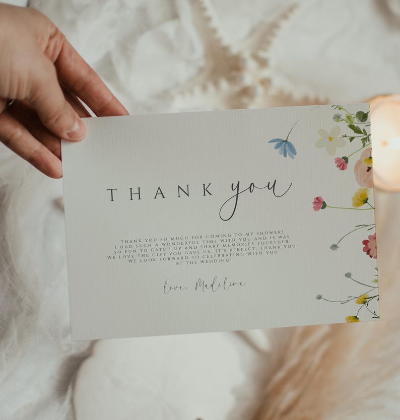 May include: A thank you card with a floral design and the text "THANK you" in a handwritten font. The card reads "Thank you so much for coming to my shower! I had such a wonderful time with you and it was so fun to catch up and share memories together. We love the gift you gave us. It's perfect. Thank you! We look forward to celebrating with you at the wedding. Love, Madeline."