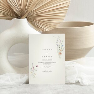 May include: A wedding invitation with a floral design featuring a bouquet of watercolor wildflowers in shades of pink, purple, and blue. The invitation reads "Lauren and Daniel" with the date and time of the wedding ceremony.
