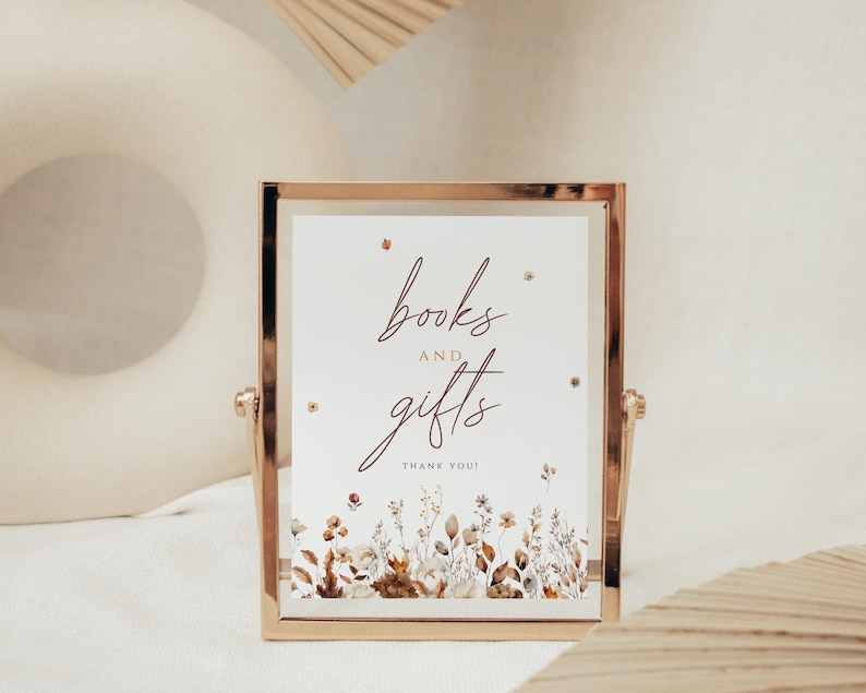 May include: A gold-framed sign with the words "books and gifts" in elegant script. The sign features a floral design at the bottom with a "Thank You!" message. The sign is displayed on a white surface.