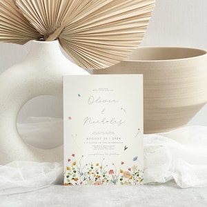 May include: A wedding invitation card with a white background and a floral border. The card features the names "Olivia & Nicholas" in cursive script and the date "August 26, 2024".
