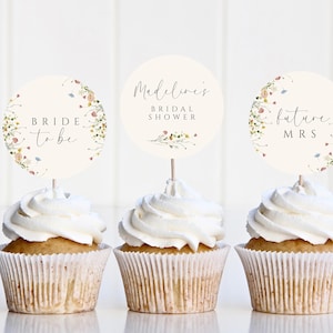 May include: Three cupcakes with white frosting topped with round paper circles. The circles have floral designs and text that reads "Bride to be", "Madeline's Bridal Shower", and "Future Mrs."